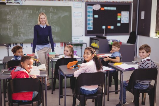 Portrait of smiling teacher and schoolkids in classroom - Powered by Adobe
