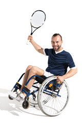 Happy young sportsman in wheelchair holding tennis racquet and smiling at camera