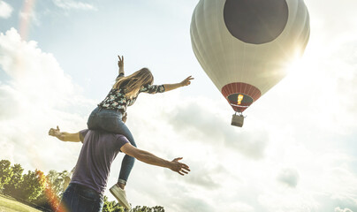Happy couple in love on honeymoon vacation cheering at hot air balloon - Summer travel concept with...