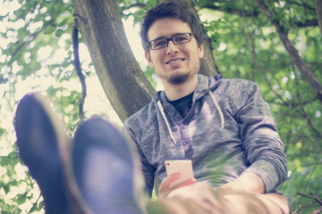 Junger Mann liegt im Gras, blickt aufs Smartphone 