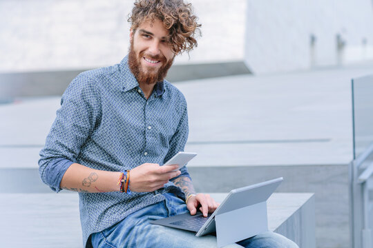 Young man with beard using a smartphone and a tablet