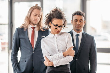 upset african american businesswoman and two businessmen standing in office, multicultural business...