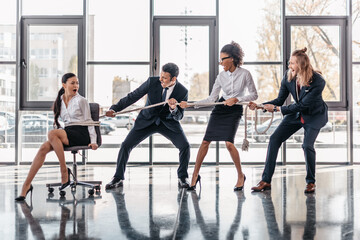asian businesswoman bound with rope on chair and multicultural business team pulling her, team spirit business concept