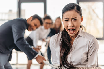 yelling asian businesswoman bound with rope and businesspeople pulling her, team spirit business concept