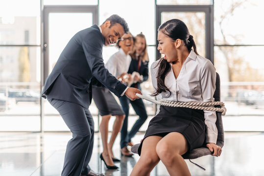 asian businesswoman bound with rope on chair and multicultural business team pulling her, team spirit business concept