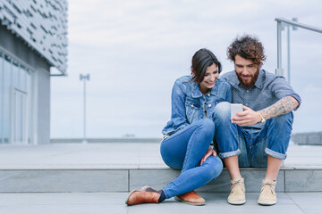 Young couple sitting on a step looking at a phone
