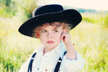 Cute boy with curly hair in black hat outdoor - beauty and fashion concept