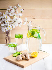 A rejuvenating drink, a cocktail, tea, water with lemon, inbet, mint, cucumber in a transparent glass and glass jug on a board on a wooden table. Improvement and cleansing of the body. Detox.