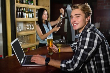 Man having beer while using laptop at bar counter