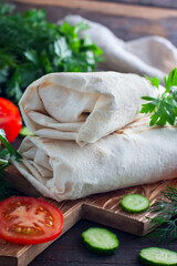 Shawarma chicken roll in a pita with fresh vegetables and cream sauce on wooden background. Selective focus
