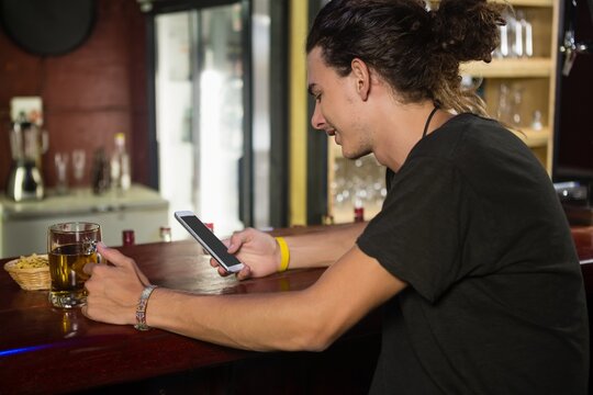 Man using mobile phone while having beer at counter
