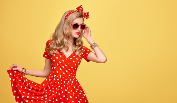 Fashion Model Girl in Polka Dots Summer Dress. Stylish Curly hairstyle, Trendy Clutch, fashion Red Headband, Sunglasses. Beauty Blond Pinup Woman in fashion pose. Glamour Playful Sexy Lady on Yellow