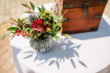 Fototapeta premium Little vase with red flowers stands before wooden chest on dinner table