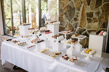 White dishes with sweets stand on long dinner table