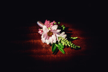 Boutonniere made of pink daisy lies on wooden table