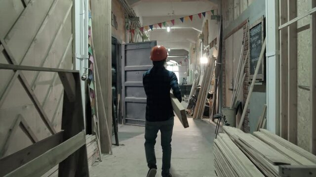 Carpenter doing his job in carpentry workshop. Man walking on factory with plywood, furniture manufacture