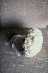 White wedding bouquet with lace ribbon lies on grey couch