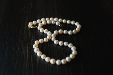 Pearl necklace lies on black wooden table