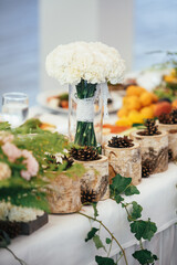 Bouquet of white flowers stands among billets of wood on dinner table