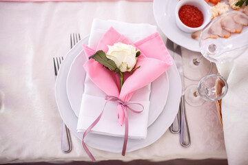 White rose lies on pink serviette on a dinner plate