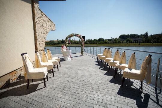 Chairs stand in the row before wedding altar on the porch over the lake