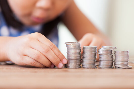 Cute asian little girl playing with coins making stacks of money,kid saving money for the future concept