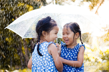 Two happy asian little girls with umbrella having fun to play with the rain together in vintage...