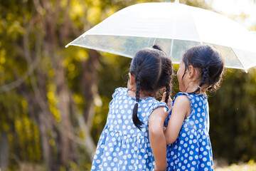 Back view of two asian little girls with umbrella having fun to play with the rain together in...
