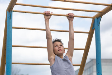 Obraz premium A teenager in a T-shirt is engaged in gymnastics on a horizontal bar