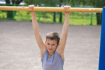 Fototapeta premium A teenager in a T-shirt is engaged in gymnastics on a horizontal bar