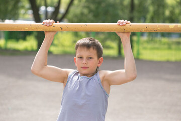 Fototapeta premium A teenager in a T-shirt is engaged in gymnastics on a horizontal bar