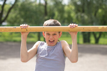 Fototapeta premium A teenager in a T-shirt is engaged in gymnastics on a horizontal bar