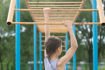 A teenager in a T-shirt is engaged in gymnastics on a horizontal bar