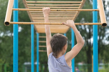 Obraz premium A teenager in a T-shirt is engaged in gymnastics on a horizontal bar