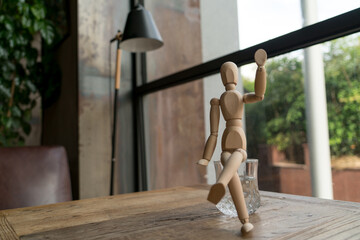 wood man is sitting on a glass of water while raise hand up