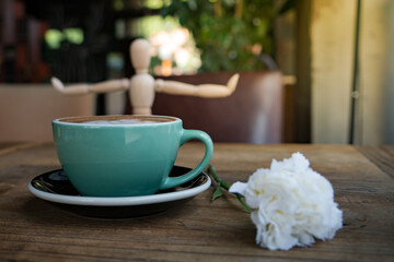 Hot mocha coffee or capuchino with white carnation flower and wood man on the wooden table