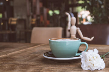 Hot mocha coffee or capuchino with white carnation flower and wood man on the wooden table
