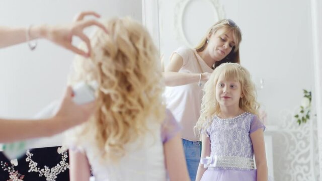 To the girl of 6 years in an elegant dress the mum does a beautiful hairdress
