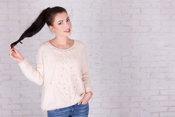 portrait of beautiful woman playing with her hair and space over white brick wall