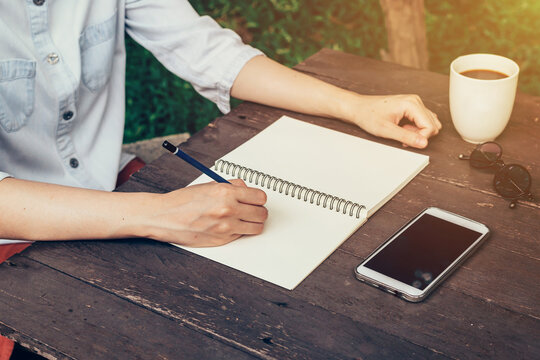 Woman hand writing note pad on wood table in coffee shop.