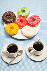 Two cups with coffee and donuts on a blue table