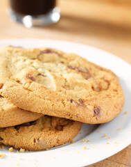 Delicious looking chocolate chip cookies on a white plate with coffee in the background