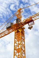 Orange construction tower crane with jib and hook isolated on blue sky with white clouds background, detail