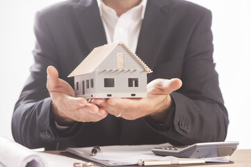 Businessman Holding Model House In Palm Of Hand