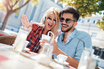 Dating. Young couple drinking coffee and having fun with mobile phone in the cafe. Love, dating, technology, lifestyle