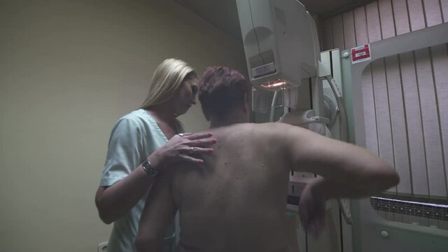 Caucasian female radiology technician set up mature woman on mammography machine, steadicam tracking shot, room interior.