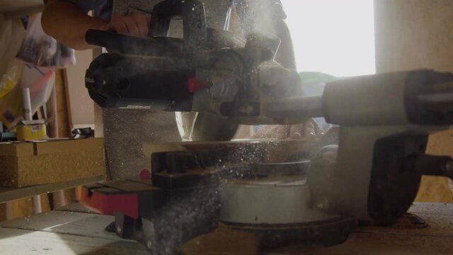 Close up hands of carpenter using circular saw. machine works with sawdust on backlight