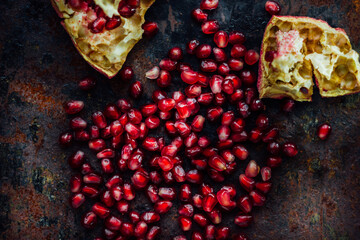 Pomegranate fruit and seeds over black rustic surface.
