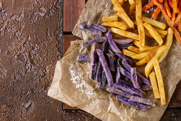 Variety of french fries traditional potatoes, purple potato, carrot served with salt on baking...