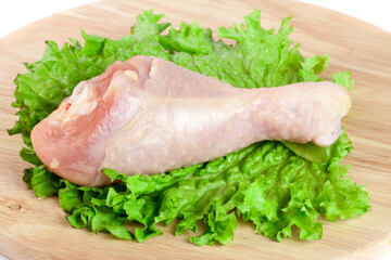 raw chicken drumstick with lettuce leaf on a wooden cutting boardn with white background